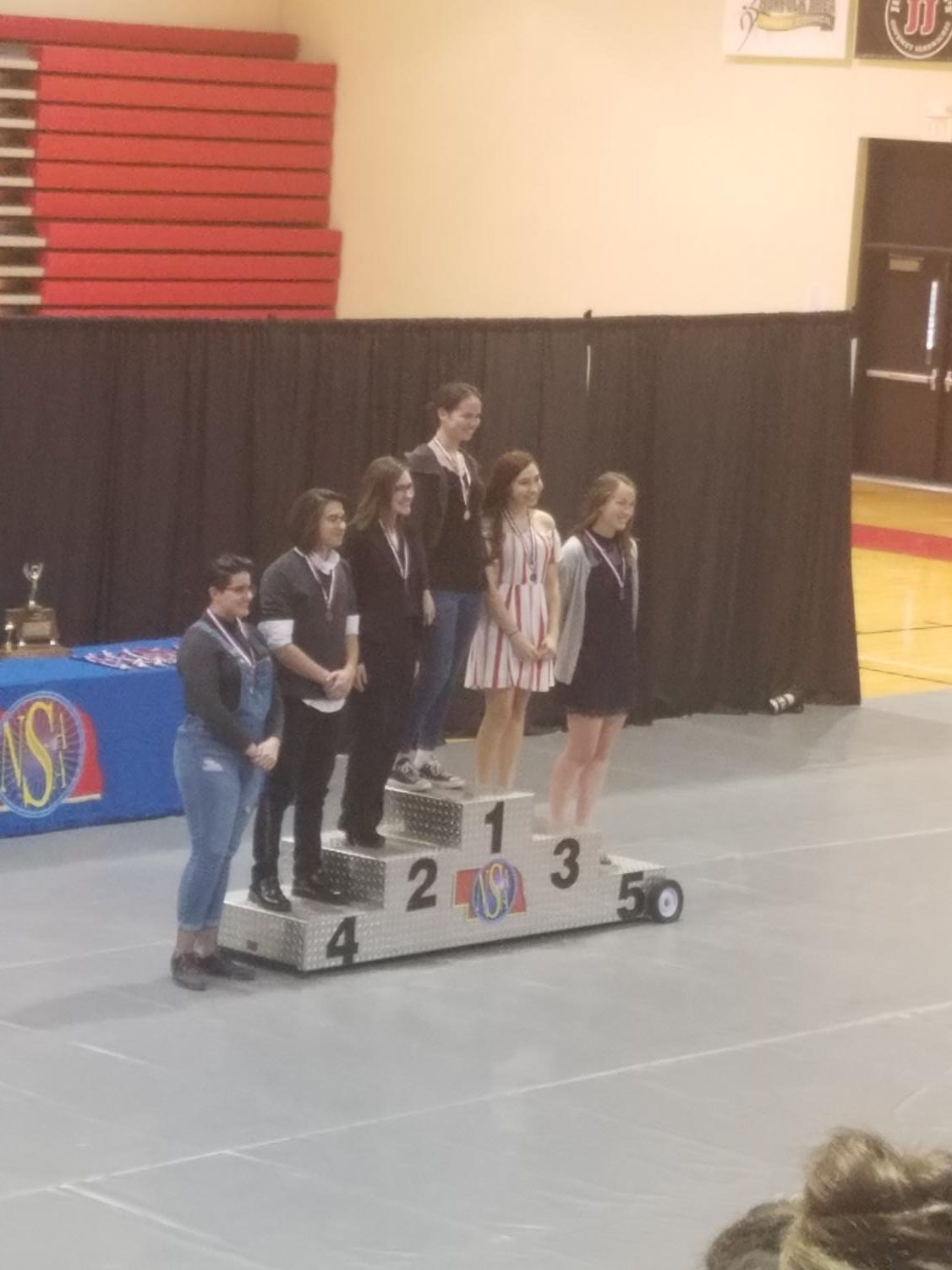 Devon Walter poses for a picture on the podium for first place, standing beside the other students who placed in the top 6 in Layout Design. Photo by Angel Trinh.
