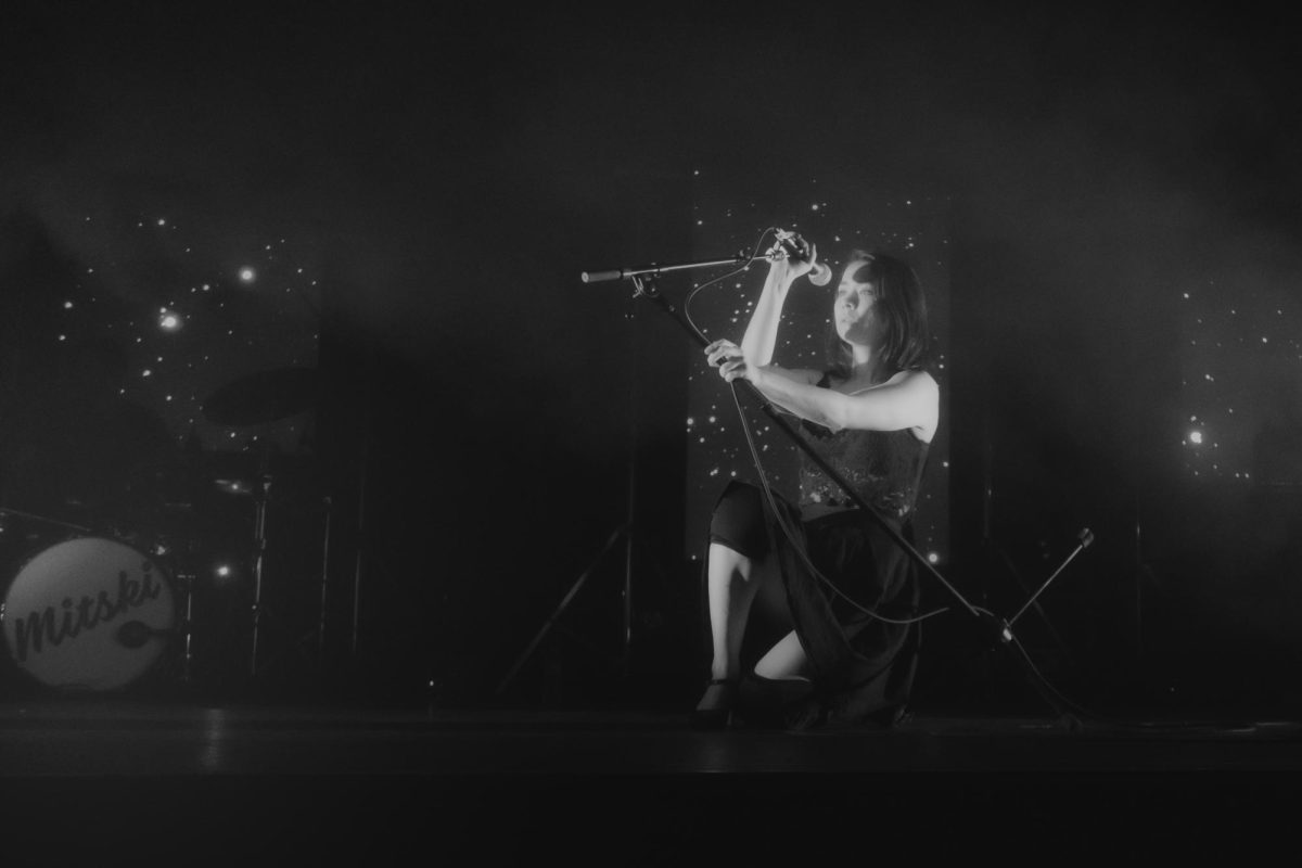 Mitski gracefully performing for an audience in black and white lighting. She is often positioned in unique and artistic poses when on stage.